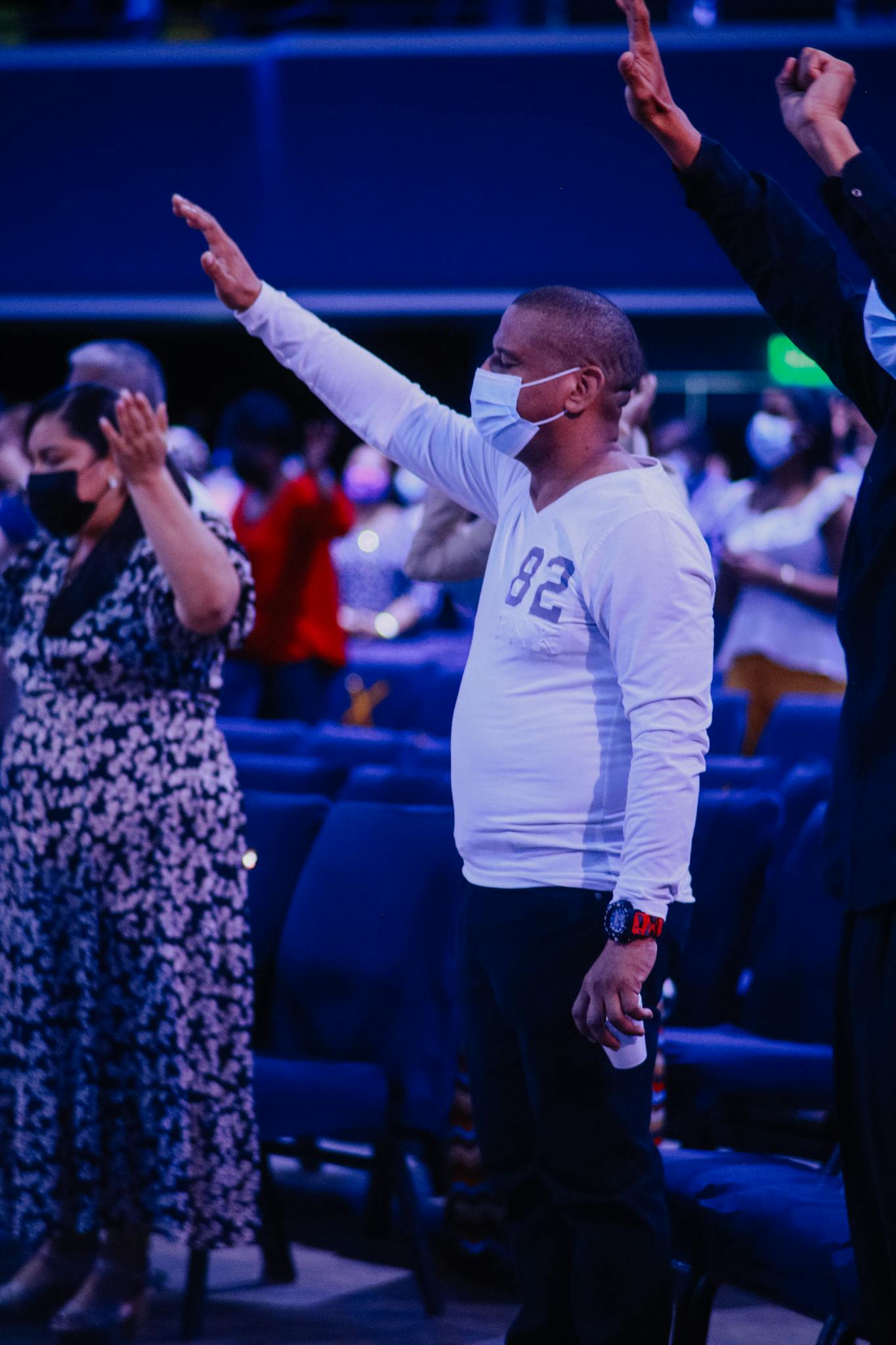 A diverse group of adults wearing masks, praying at an indoor worship service.