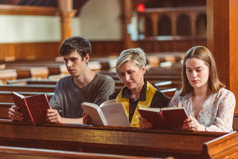 Three individuals reading bibles together in a church setting.
